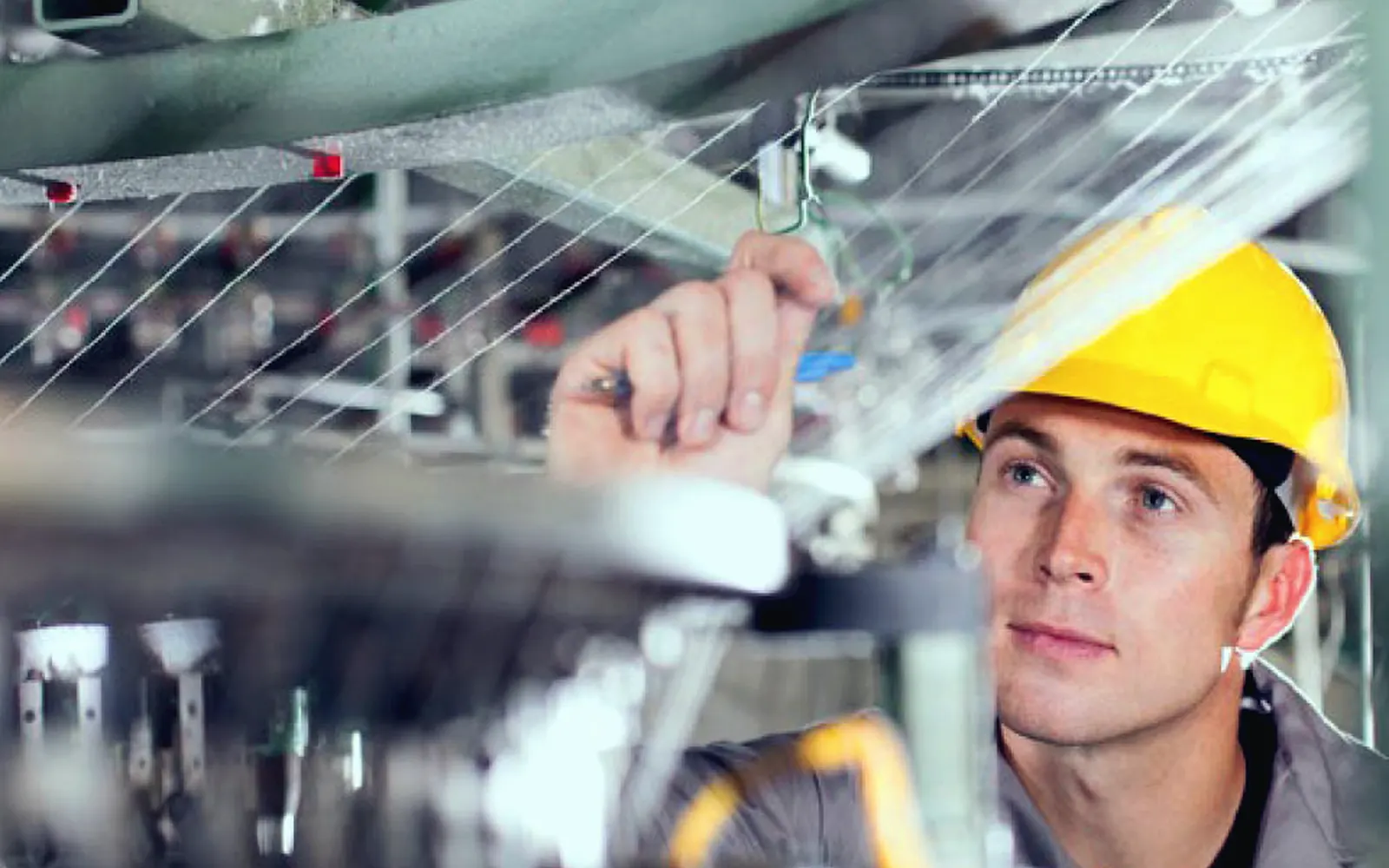 Técnico de capacete amarelo ajustando uma máquina têxtil no chão de fábrica
